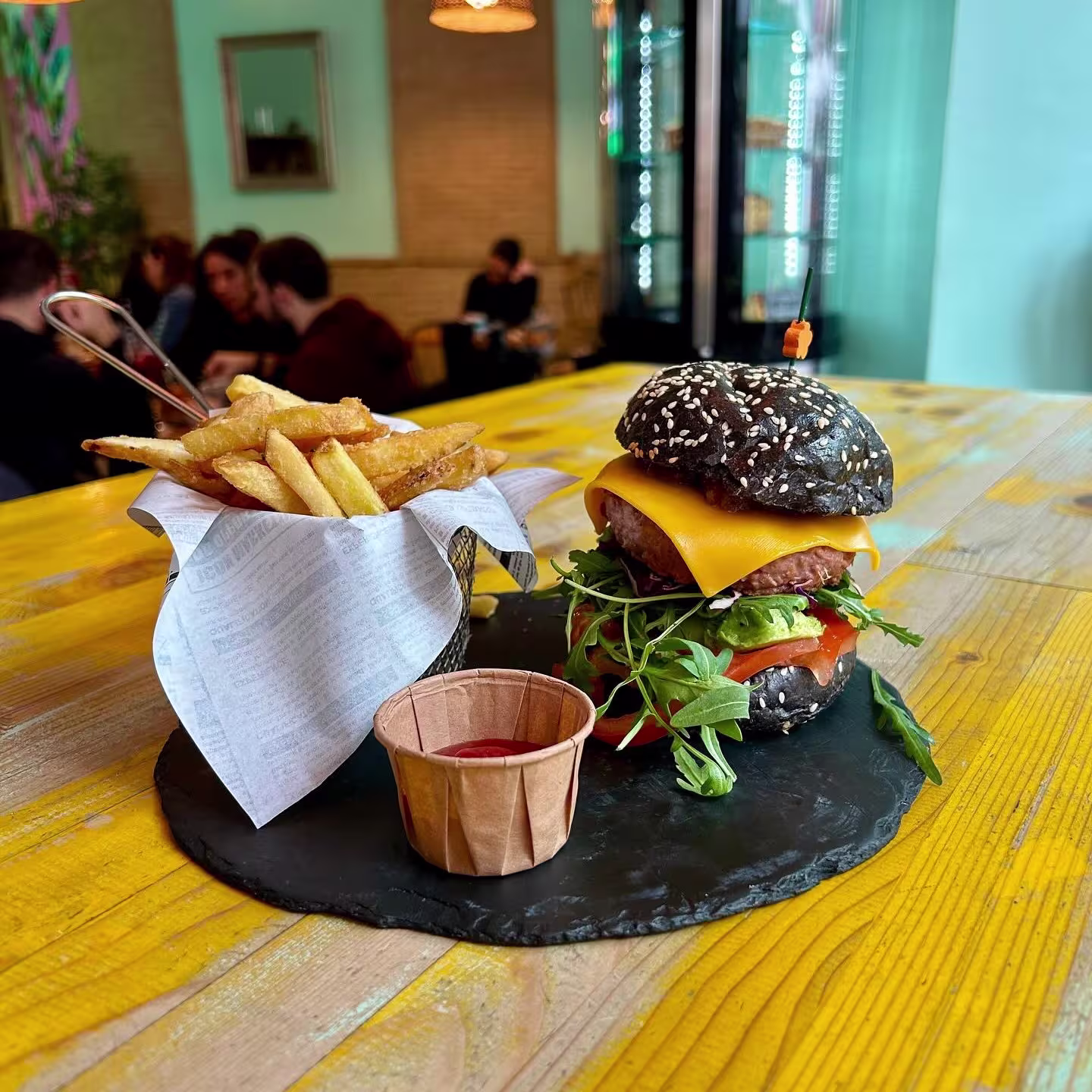Plato de La Mala Brunch con hamburguesa de pan negro, queso cheddar, lechuga, tomate, papas fritas y salsa sobre bandeja de pizarra.
