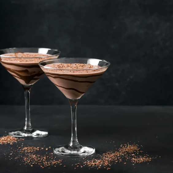 Dos copas de martini con cócteles con chocolate y cacao rallado alrededor