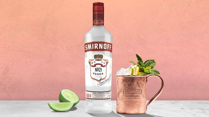 La imagen muestra una botella de vodka Smirnoff, un vaso de cobre con el cóctel Moscow Mule y una rodaja de limón.