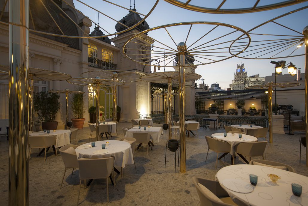 Terraza del Casino de Madrid, con mesas elegantes, sillas cómodas y sombrillas metálicas, ofreciendo vistas panorámicas al atardecer.