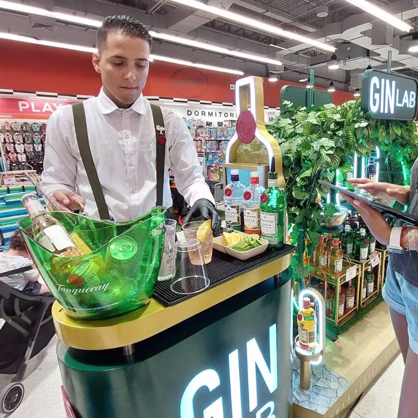 En la imagen de se de lado derecho a la persona con la tablet participando del evento y del derecho al bartender armando un cóctel. De fondo se ve el stand circular.