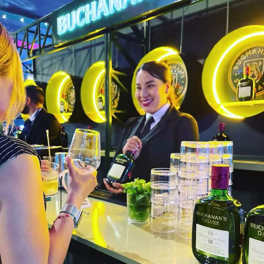 En la imagen de se a Esteffany detrás de la barra, asistiendo a un cliente mostrando la botella de Buchanan´s