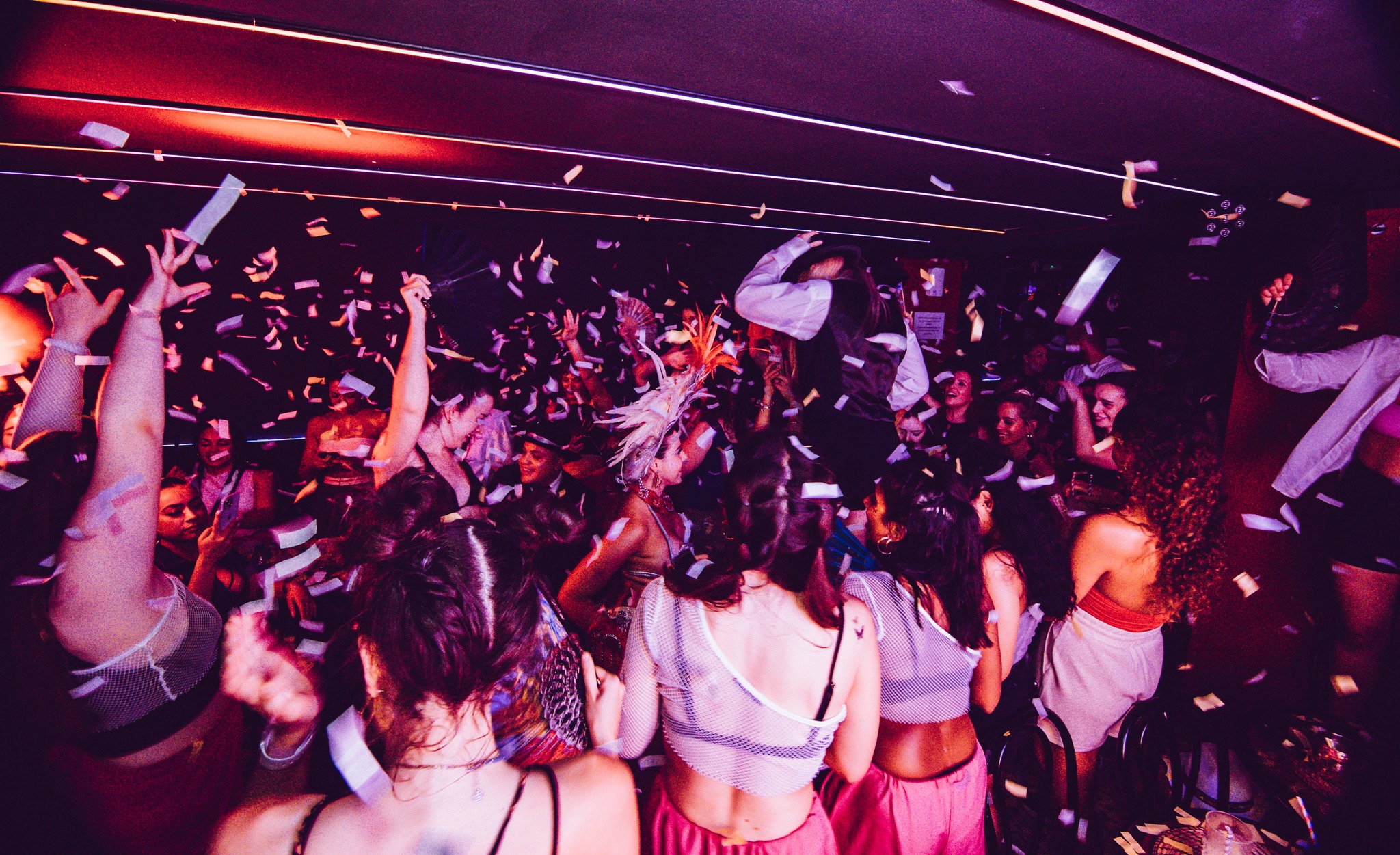 Karnaval Music Bar con una multitud vibrante celebrando bajo lluvia de confeti en una fiesta llena de energía y color.