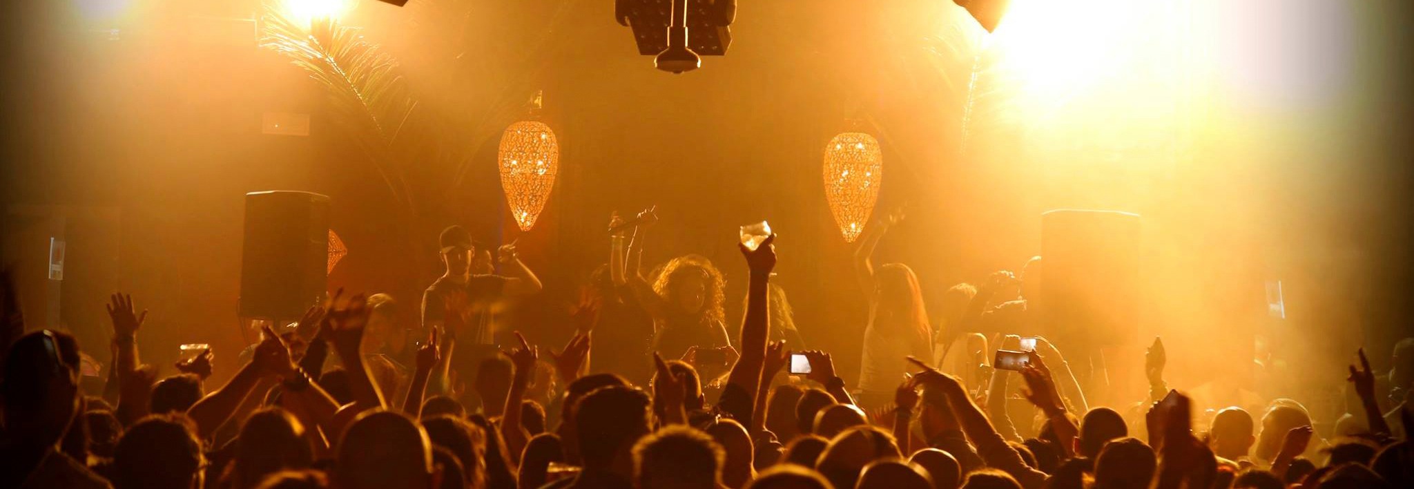 Fiesta en Kumarah con iluminación cálida, candelabros brillantes y una multitud disfrutando de la música en un ambiente vibrante
