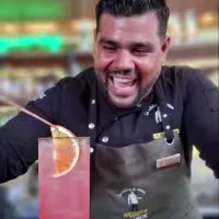 En la imagen se ve a un bartender expresando felicidad preparando un cóctel sobre la barra.