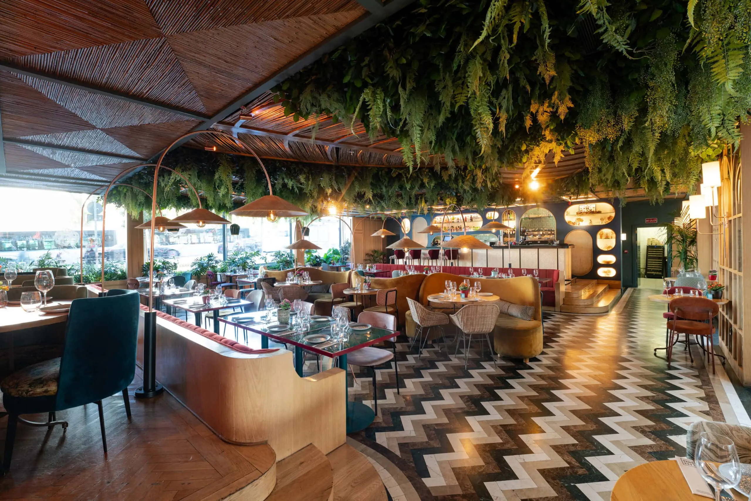 Interior de Botania con techo decorado de vegetación, mesas elegantes y ambiente acogedor que mezcla diseño natural y contemporáneo.