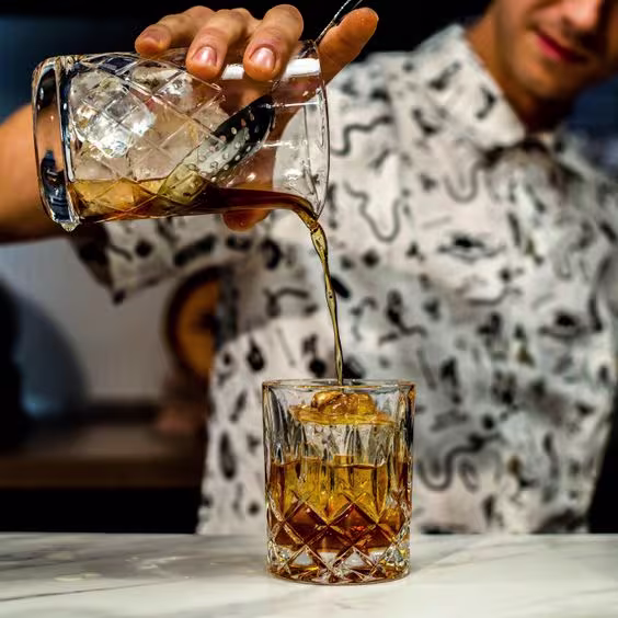 La imagen muestra a un chico vertiendo un cóctel desde un vaso a otro.