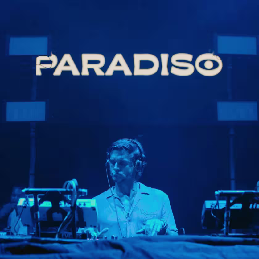 Imagen de DJ tocando con luces azules. Logo Paraiso por encima de su cabeza.