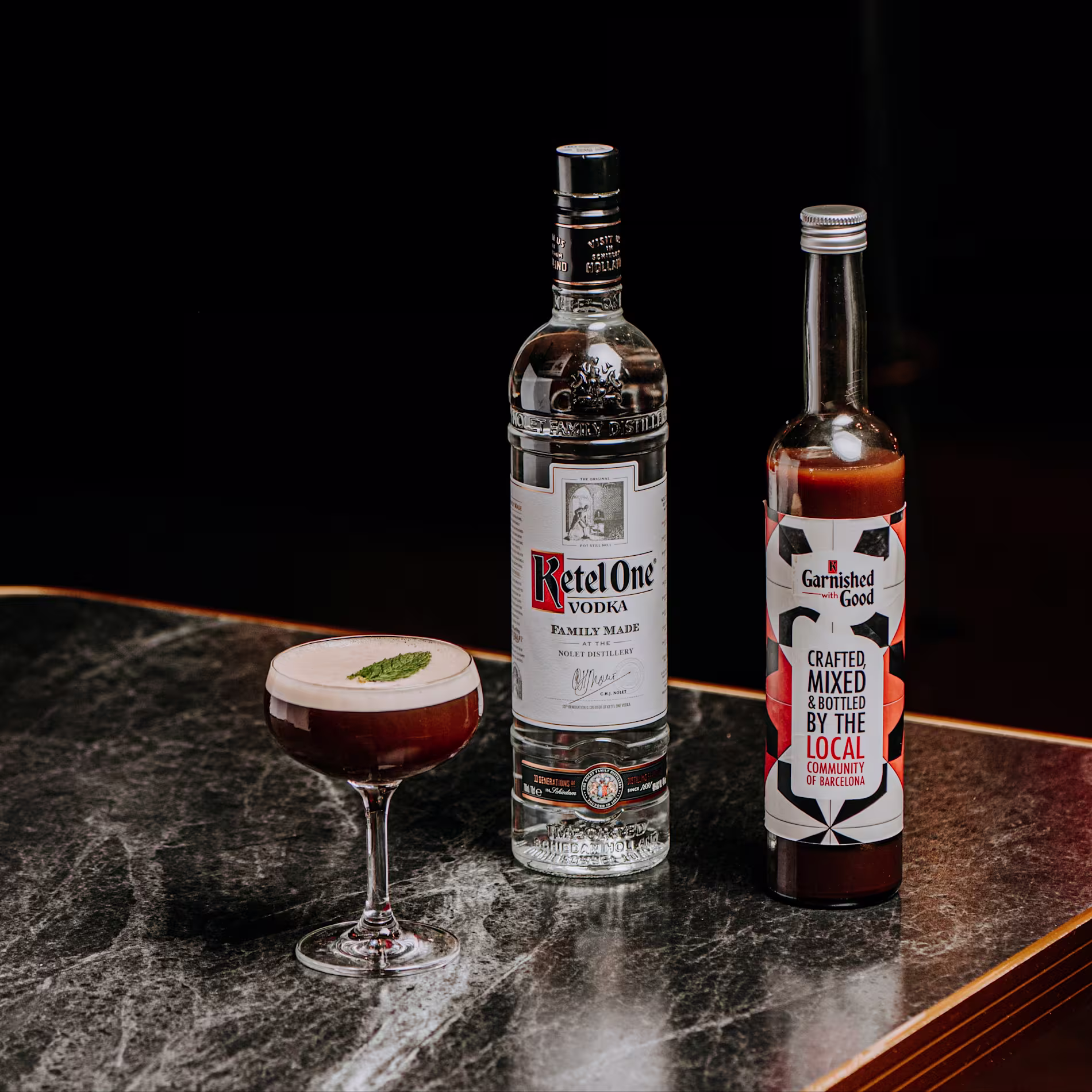 Cóctel artesanal con Ketel One y Garnished with Good sobre mármol oscuro, coronado con menta. Elegancia y sabor en cada detalle.