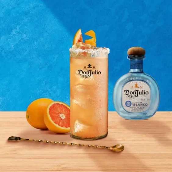 Cóctel Don Paloma junto a una botella de Don Julio Blanco, una toronja y media cortada y un batidor.