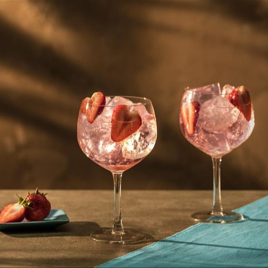 Two pink gin cocktails with sliced strawberry garnishes on a brown and blue table.