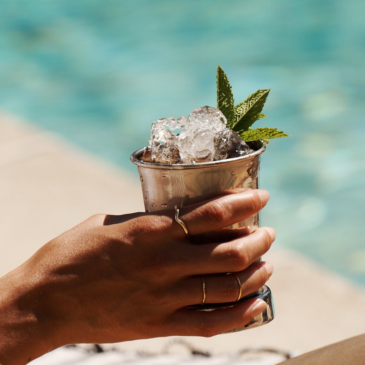 A Mint Julep cocktail held by a woman sitting next to a pool