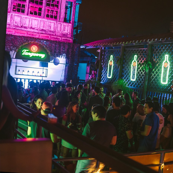 Gente en discoteca al aire libre. Luces al rededor con logo de Tanqueray