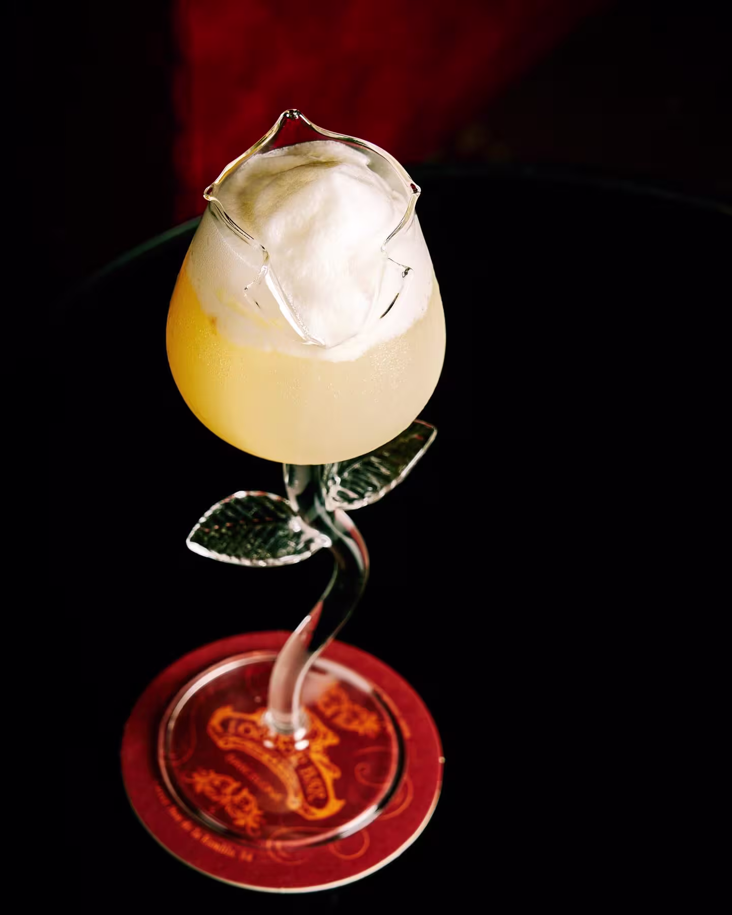 Cóctel exclusivo en London Bar servido en copa con forma de flor, espuma en la parte superior y base decorada con hojas de cristal.
