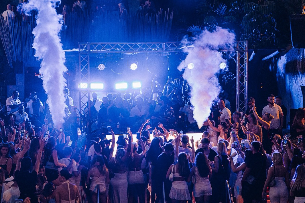 Fiesta en Mogli The Key con efectos de humo, luces vibrantes y asistentes disfrutando de un ambiente exclusivo al aire libre.