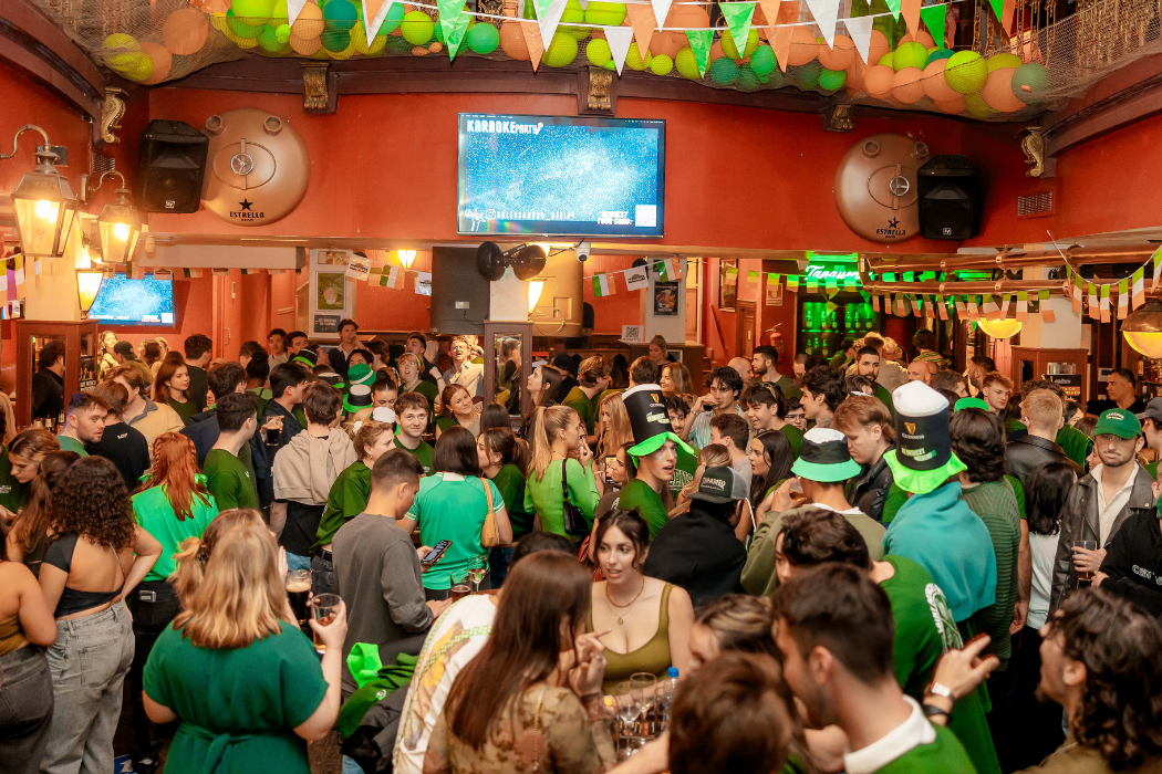 La imagen muestra el espacio interior del George Pain, celebrando un evento. La mayoría de las personas visten de verde, lo que podría sugerir que la celebración está relacionada con el Día de San Patricio.