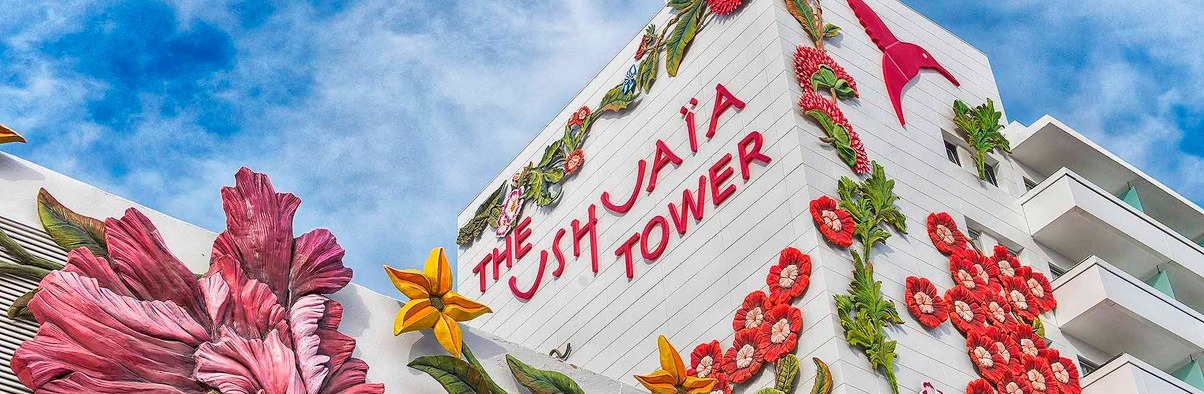 Fachada de The Ushuaïa Tower decorada con grandes flores coloridas y el logotipo característico, destacando sobre un cielo azul vibrante.