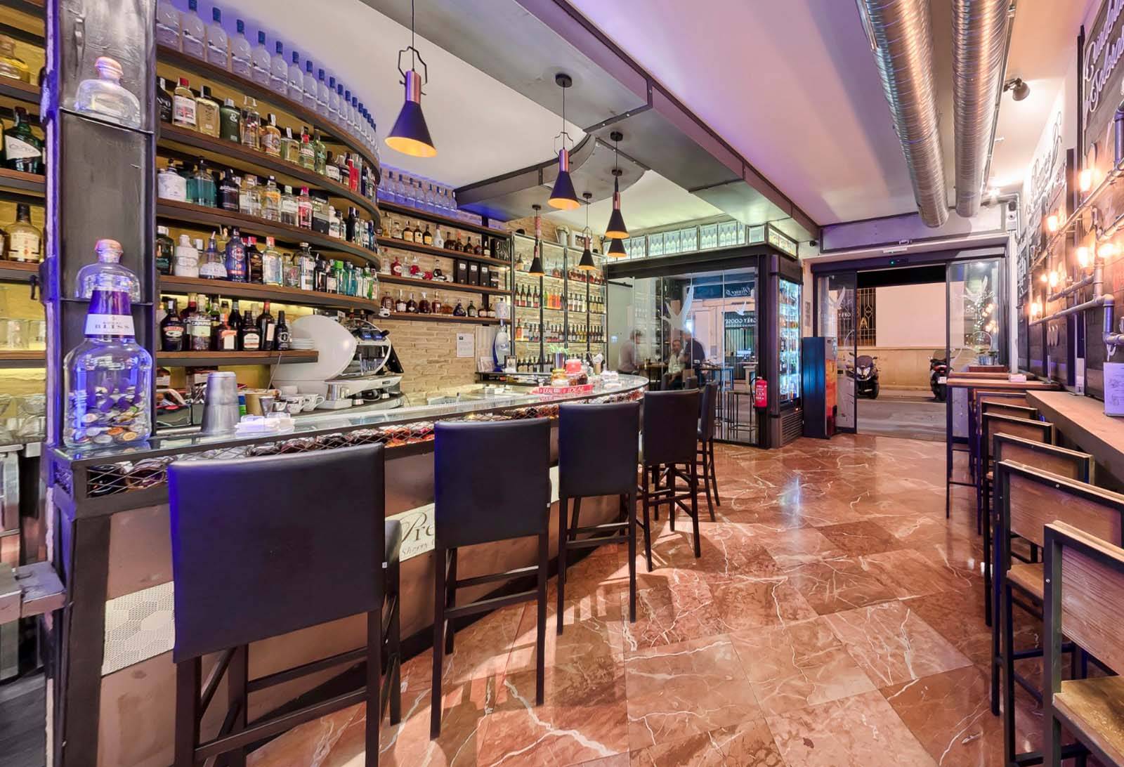 Barra de Sherry Cocktail Bar con botellas exhibidas, iluminación moderna y detalles industriales en un ambiente acogedor.