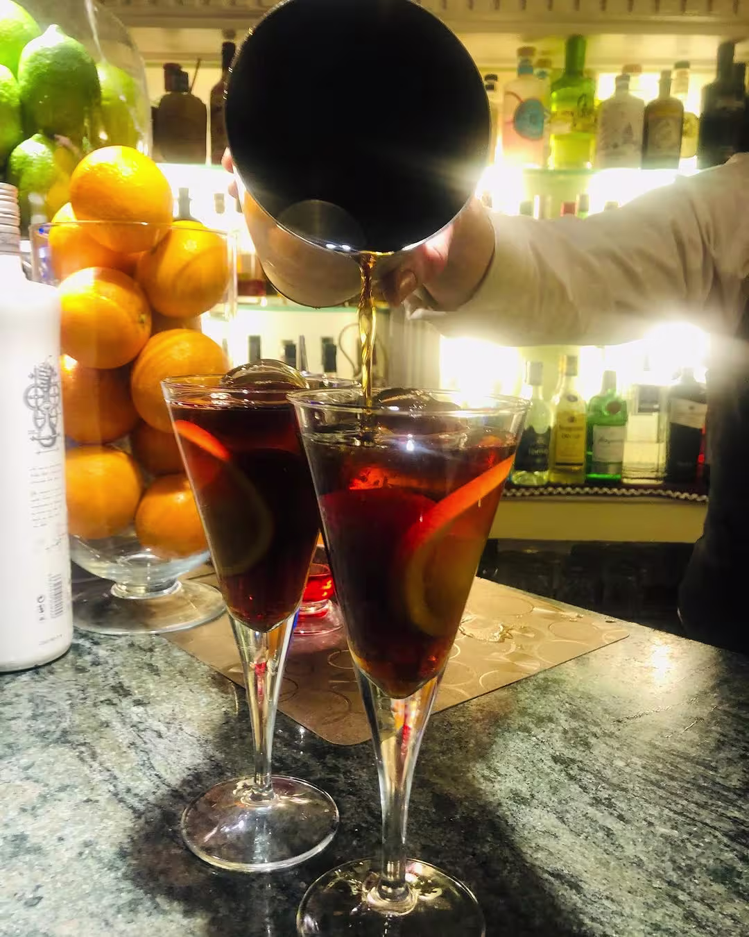 Interior del Bar Jaime dos copas de vermut servido con rodajas de limón, mientras el camarero añade el toque final desde una coctelera.