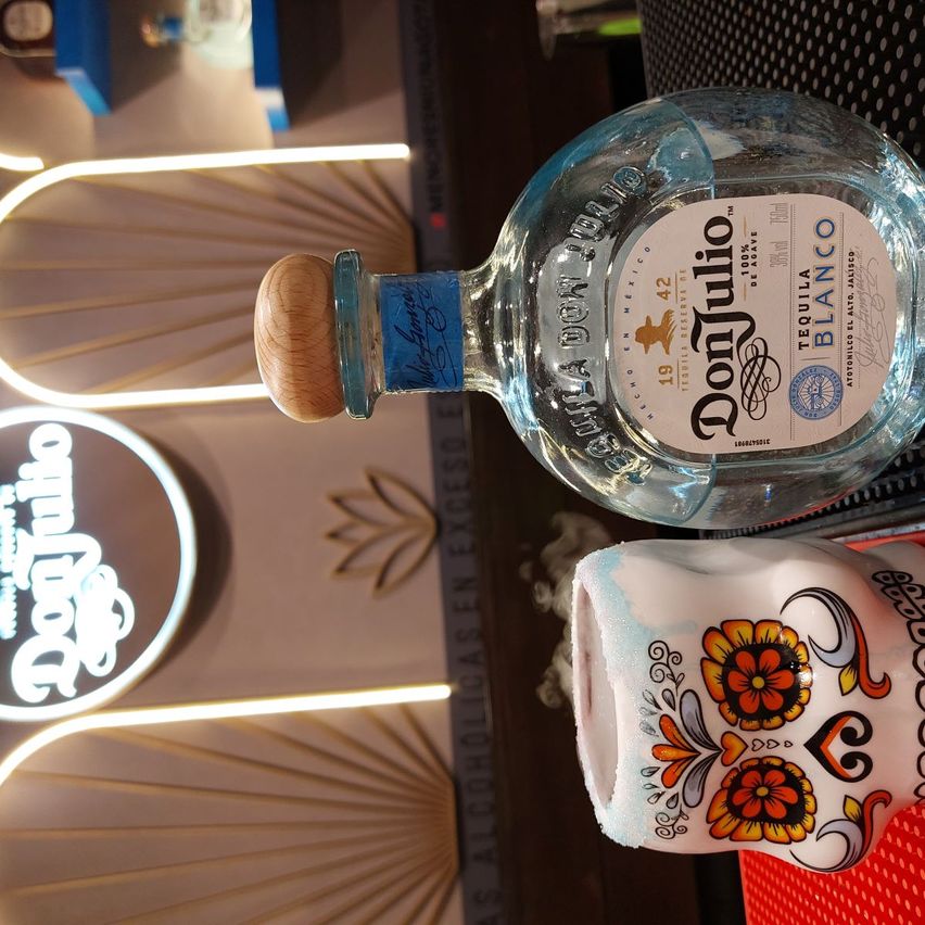en la imagen se ve la botella de Don Julio Blanco sobre la barra, junto con el vaso del cóctel q es una carabela pintada al estilo mexicano