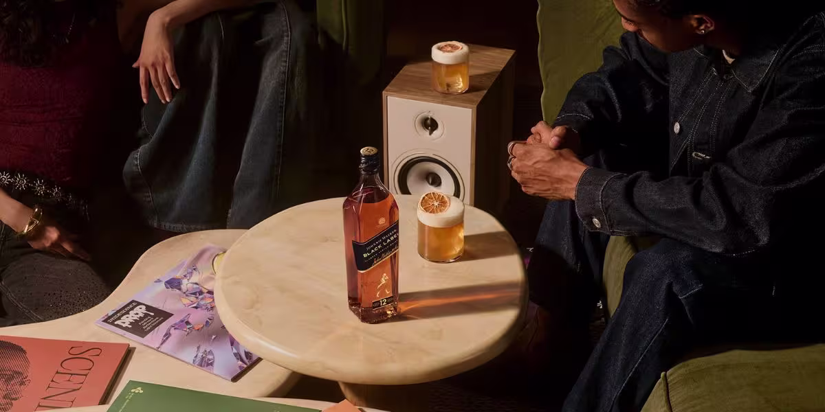 A group of people seated at a bar raise their glasses of a light-colored drink in a celebratory toast.