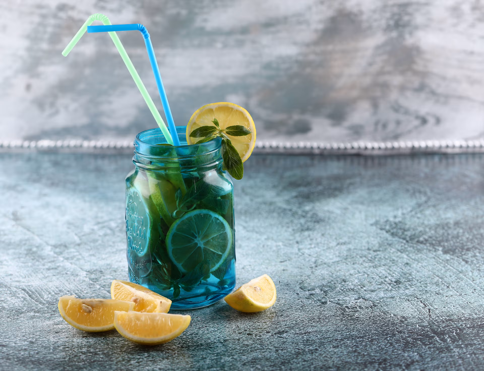 Blueberry Mojito cocktail on counter top surrounded by lemon slices 