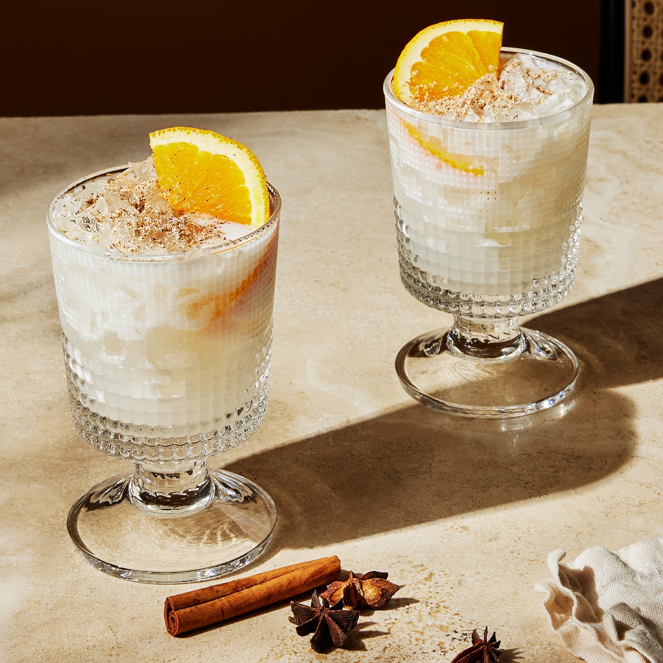 Two autumn cocktails with orange slice garnishes next to cinnamon sticks and star anise.