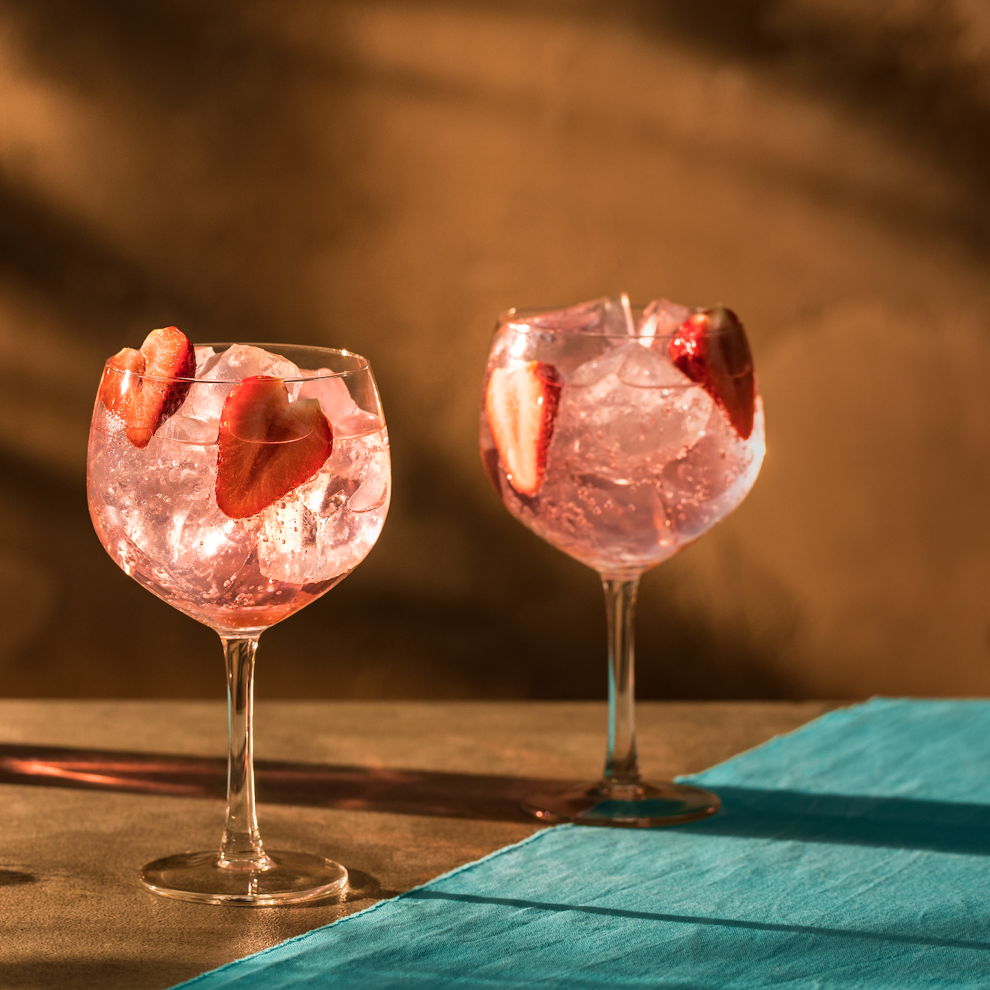 Two pink gin cocktails with strawberry garnishes.