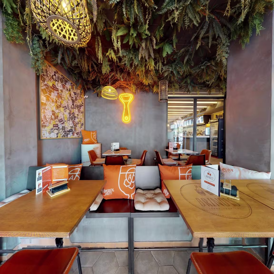 Brindis: Ambiente acogedor con decoración de neón y toques verdes que aportan frescura. Los asientos y mesas en tonos cálidos crean un espacio perfecto para socializar mientras disfrutas de un aperitivo o cóctel.