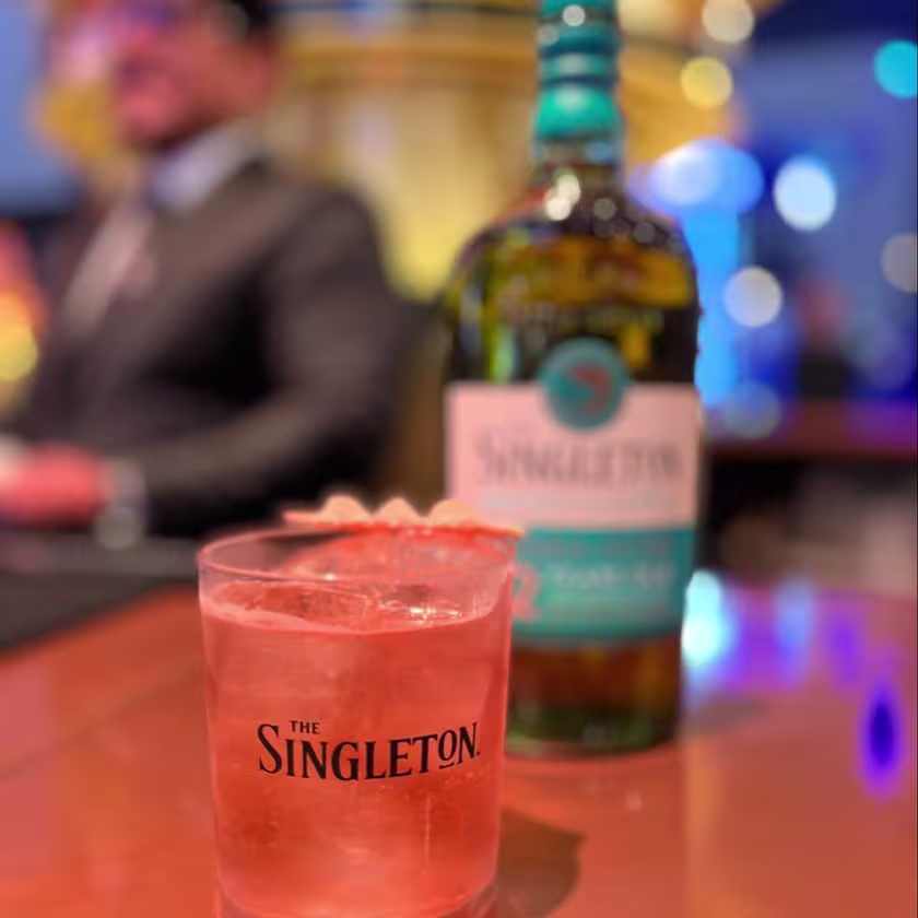 En la imagen se ve un vaso con logo Singleton con un coctel y la botella detrás.