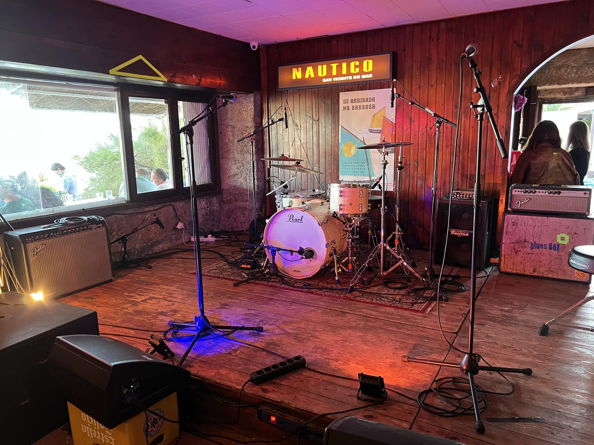 La imagen muestra el escenario de Náutico de San Vicente, un lugar acogedor con decoración rústica en madera. Equipado con instrumentos y amplificadores, el ambiente refleja una atmósfera íntima, perfecta para presentaciones musicales en vivo.
