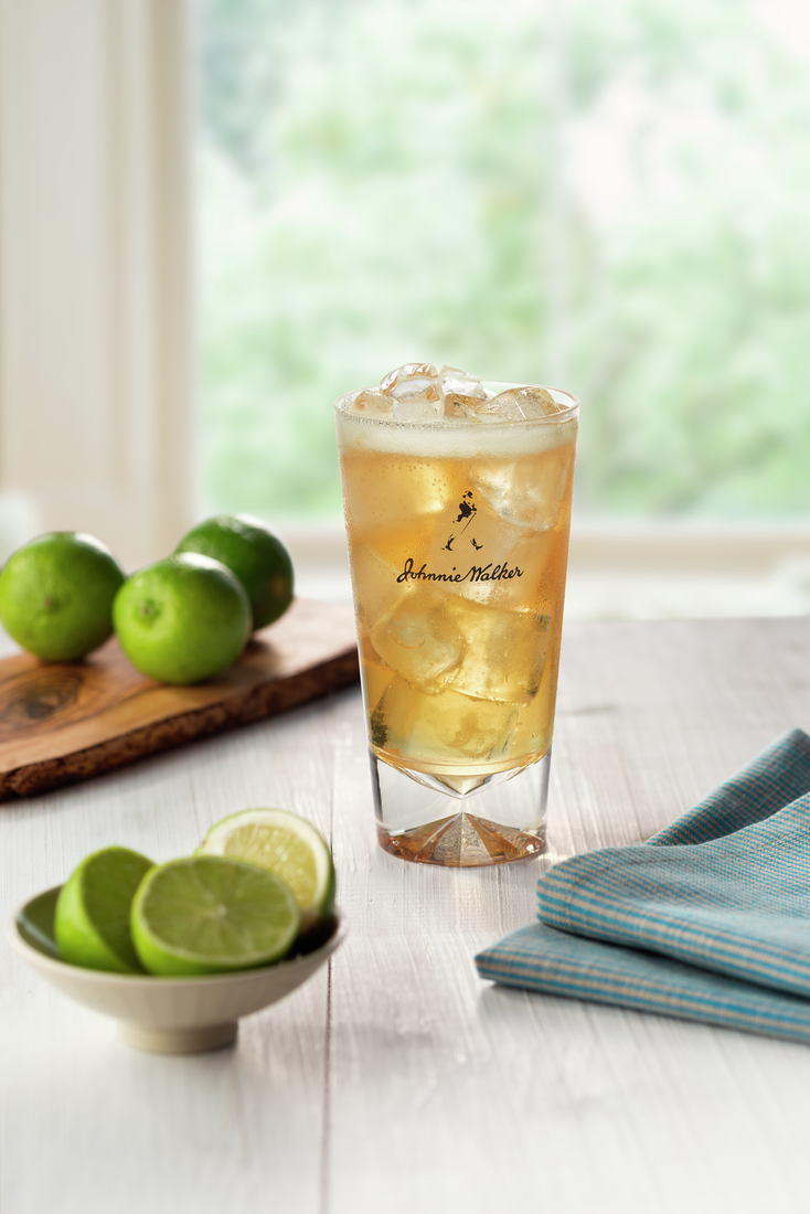 La imagen muestra un vaso con un cóctel preparado con whisky Johnnie Walker, con limones dispuestos alrededor.