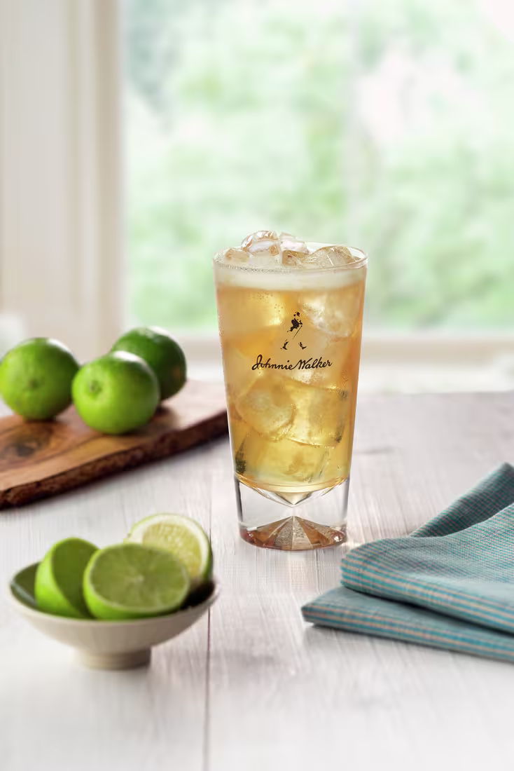 La imagen muestra un vaso con un cóctel preparado con whisky Johnnie Walker, con limones dispuestos alrededor.