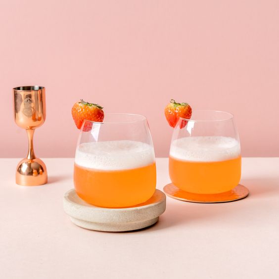 Dos vasos con un cocktail anaranjado y una frutilla como decoración.