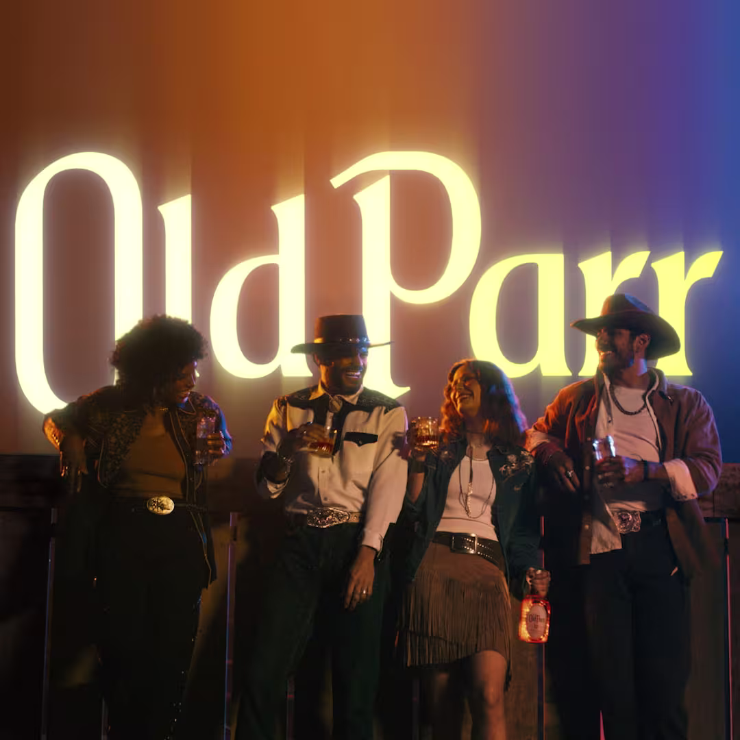 Grupo de amigos brindando con Whisky Old Parr frente a letrero luminoso de la marca
