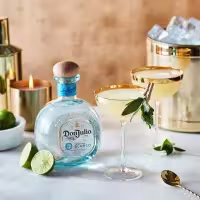 La imagen muestra una botella de tequila Don Julio Blanco junto a dos copas rellenas con el cóctel Margarita y otros elementos de coctelería alrededor.