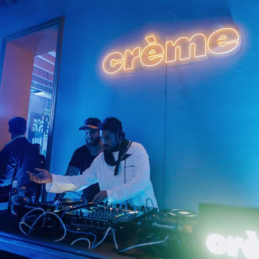 En la imagen de se un DJ pasando música con el logo de Creme detrás en luces de neón