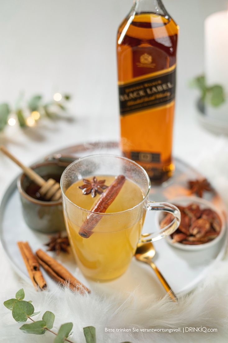 La imagen muestra una botella de whisky Johnnie Walker Black Label y una taza con el cóctel Whisky Hot Toddy.