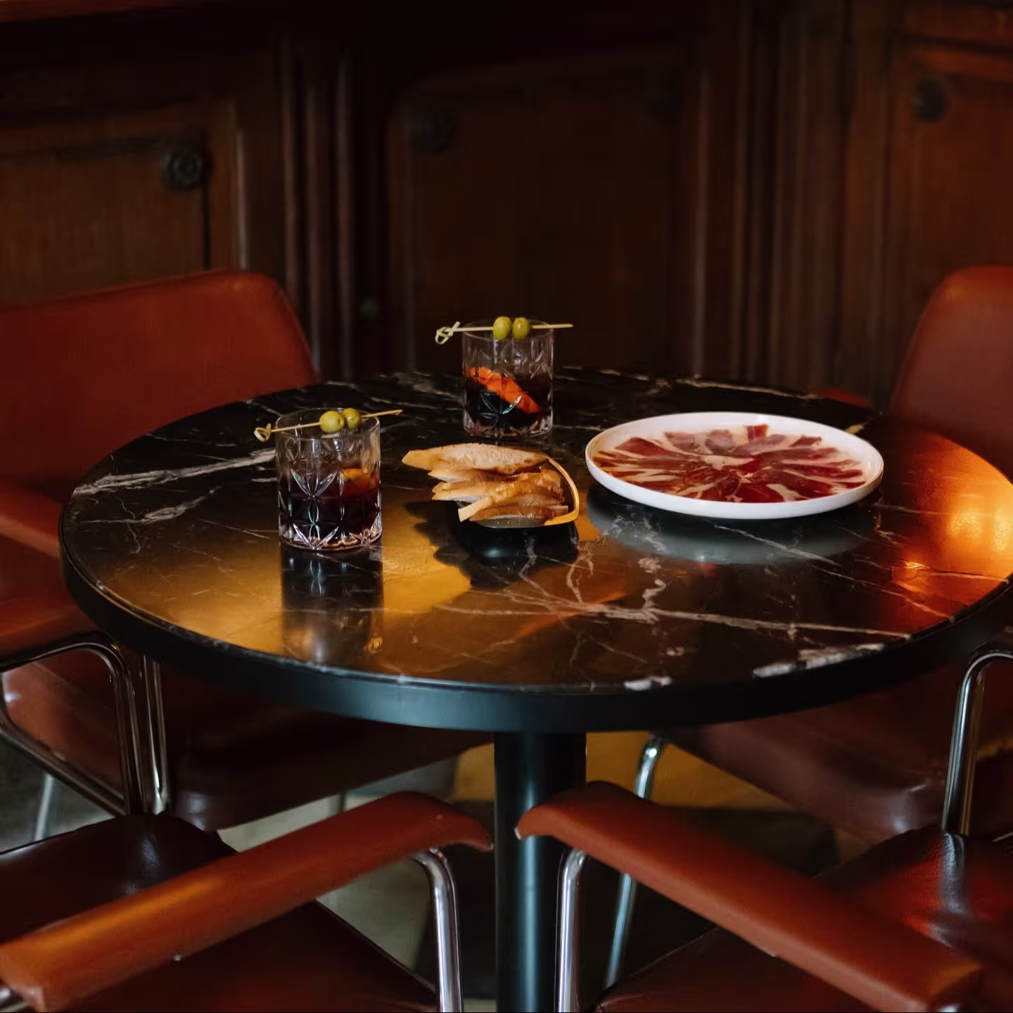 Gran Martínez propone una mesa elegante con vermuts, jamón y patatas, en un entorno clásico de madera y mármol que invita a saborear sin prisa.
