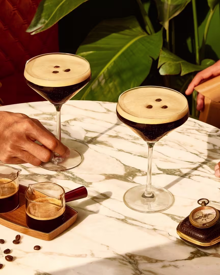 Two espresso martini cocktails on a table with two people.