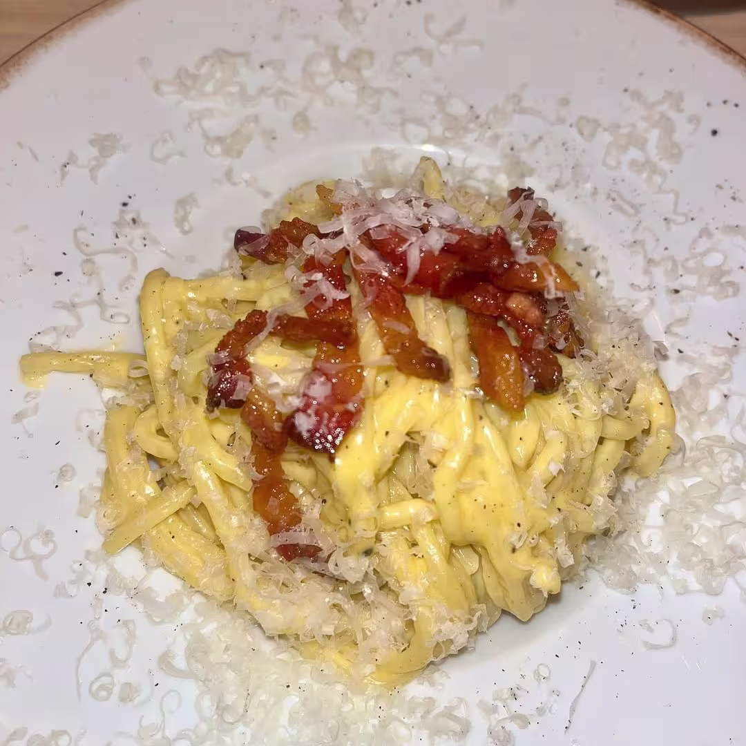 Pasta carbonara con salsa cremosa, guanciale crujiente y queso rallado, servida con un toque de pimienta en un plato de estilo rústico.