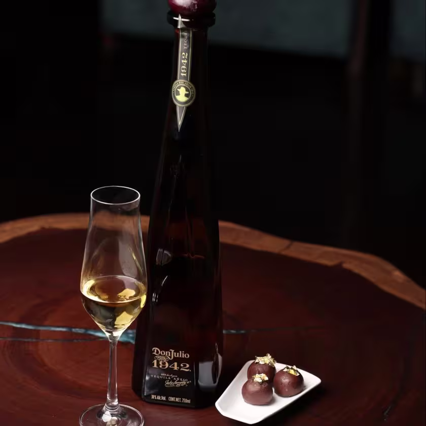 La imagen muestra una botella de Tequila Don Julio 1942 junto a una copa con el cóctel "1942 Encore", y al lado, tres trufas de chocolate.