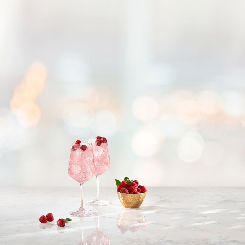 La imagen muestra dos copas con cócteles preparados con vodka Smirnoff Raspberry, junto con un bol con frambuesas.