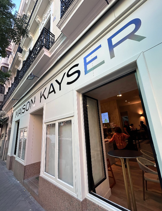 Fachada blanca con ventanales abiertos, mesas altas y ambiente acogedor en Maison Kayser Zurbano.