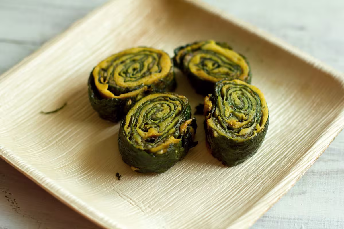 Four pieces of rolled leafy green and yellow snack arranged on a square beige plate.