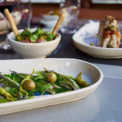 Los Madriles Taberna presenta platos tradicionales reinventados con mimo, como estas sardinas en escabeche con aceitunas, en una vajilla artesanal que realza su esencia castiza.