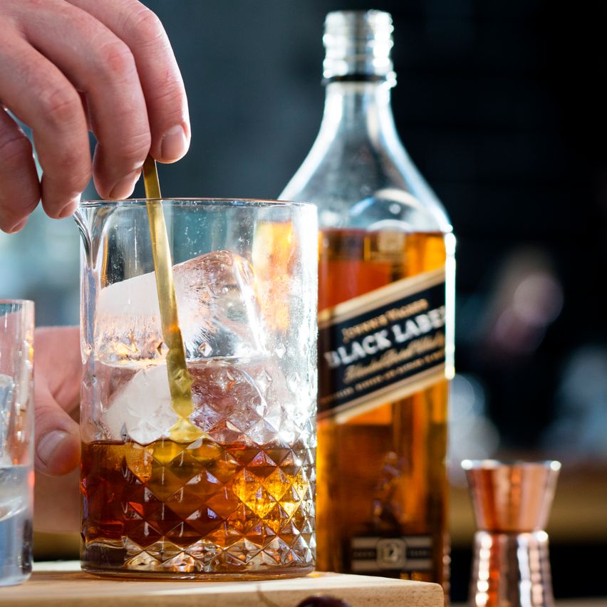 La imagen muestra una mesa con una variedad de platos de comida, destacando en el centro una botella de tequila Don Julio Blanco, mientras que dos personas brindan con cócteles Margarita.