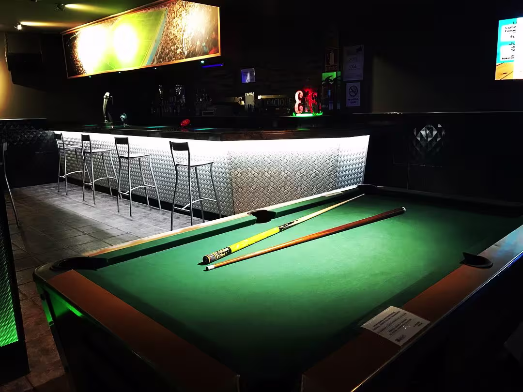 Mesa de billar en Parkim Bar con barra iluminada al fondo y sillas metálicas. Ambiente deportivo y relajado para disfrutar con amigos.