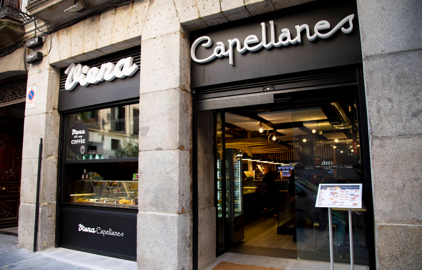 Fachada moderna en piedra y negro de Viena Capellanes Bordadores, con escaparate de dulces y acceso directo a un interior contemporáneo.