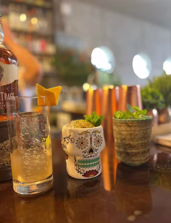 En la imagen se ven 3 cócteles sobre la barra. El cóctel del medio es un vaso con forma de calavera.